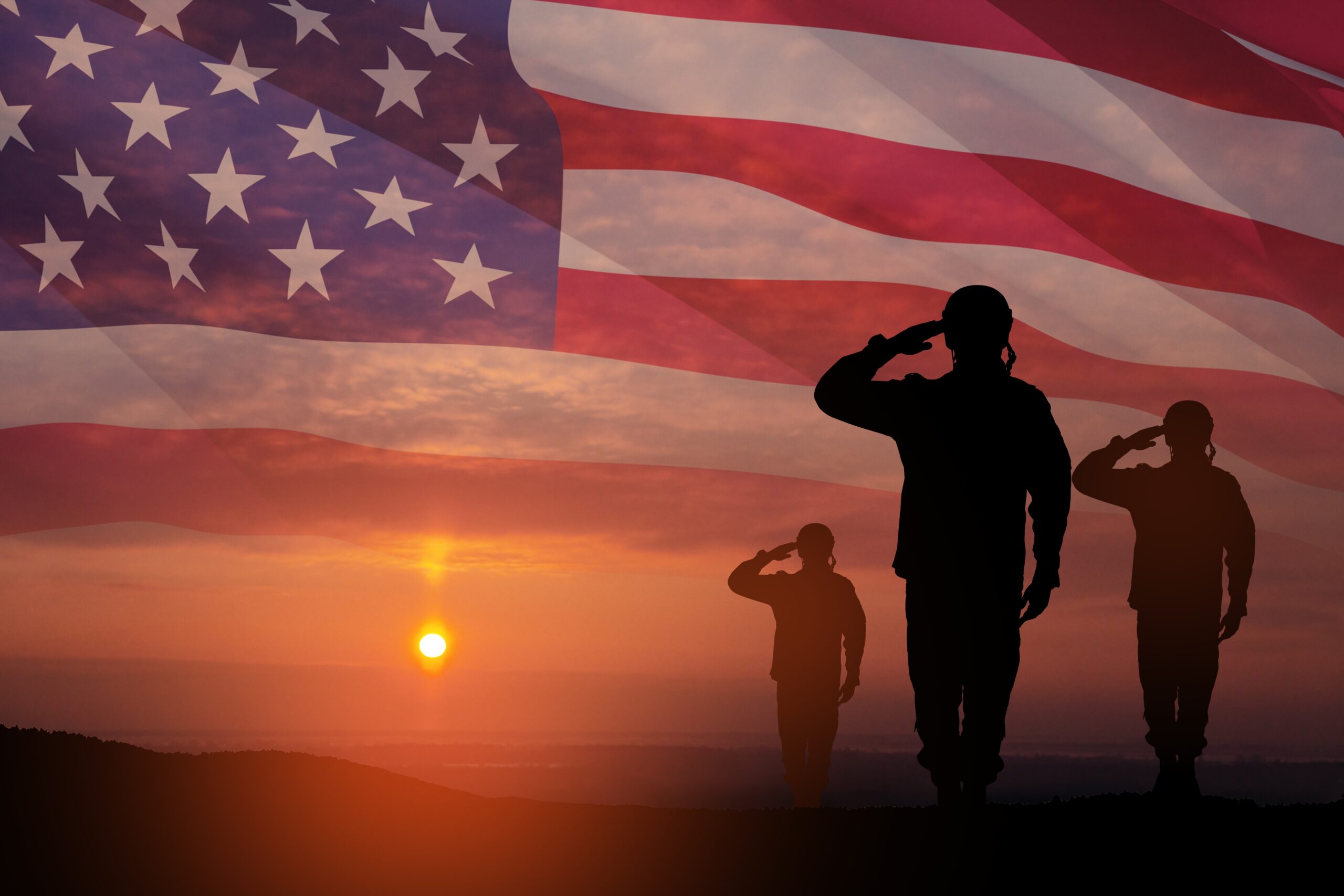 Silhouetted soldiers saluting at sunset with a large American flag blended into the sky background.